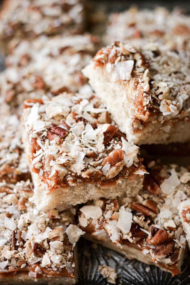 Caramel pecan coconut shortbread bars stacked on a baking sheet.