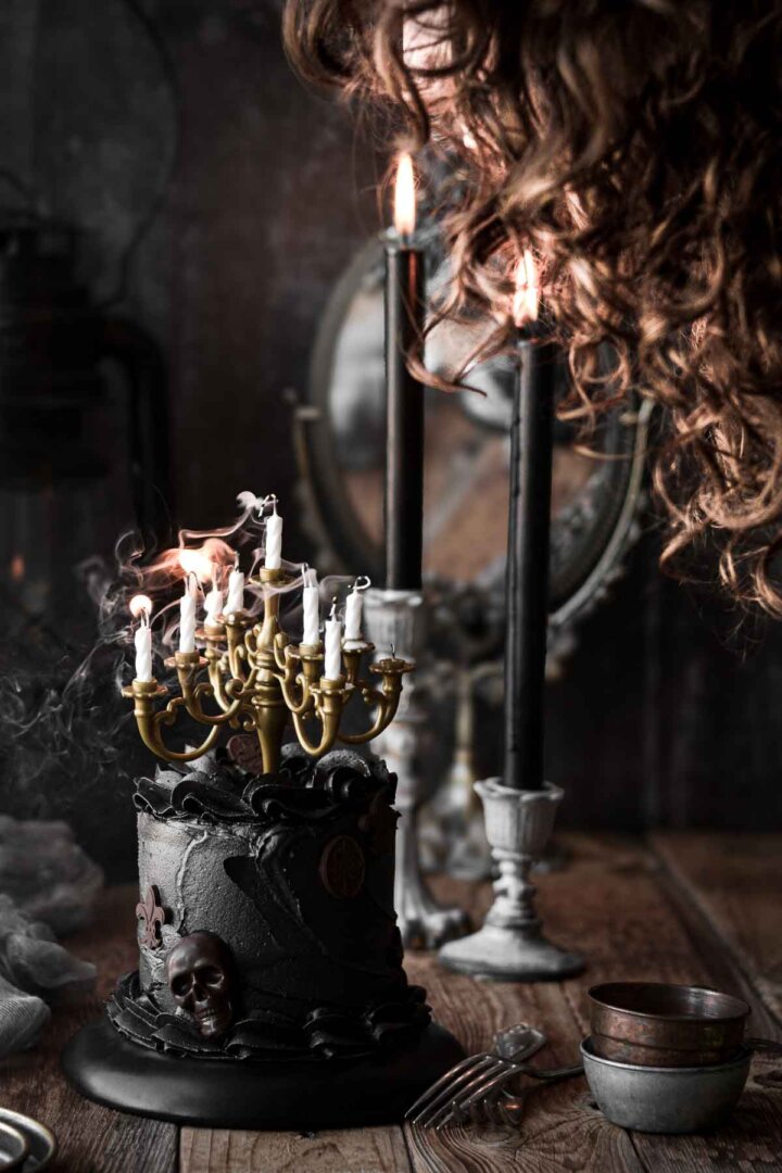 Candles being blown out on top of a black Halloween cake.