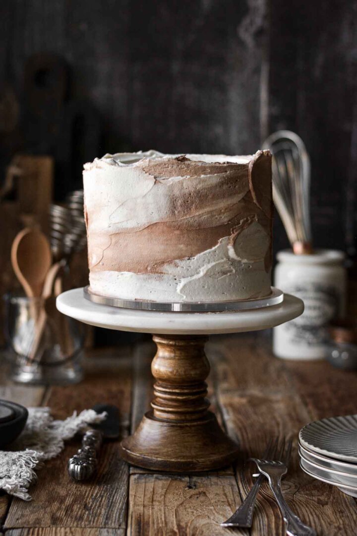 Coffee ginger cake with white and brown swirled buttercream on a wood and marble cake stand.
