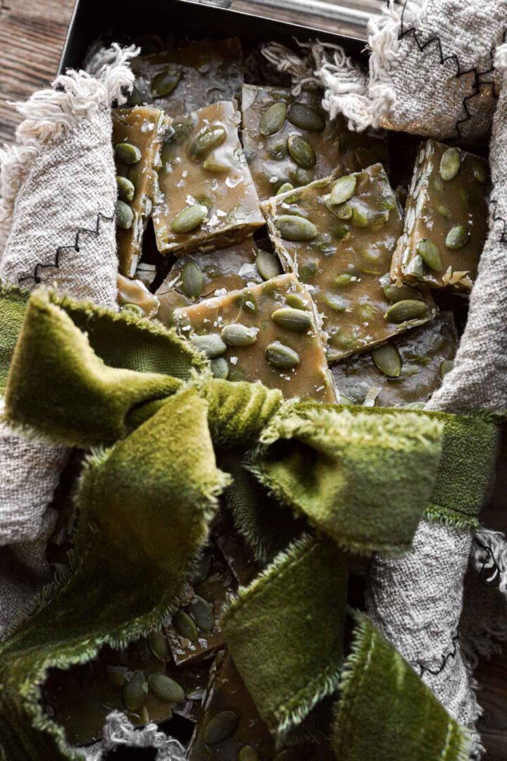 A green ribbon tied around a tin of pumpkin seed toffee.