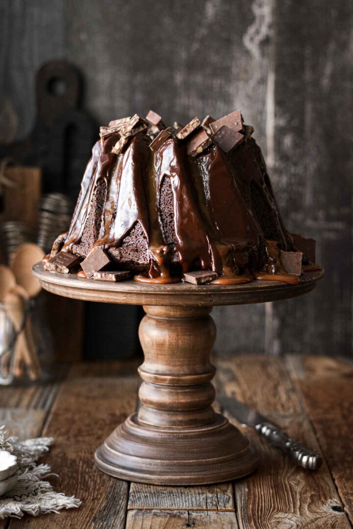 Chocolate caramel bundt cake on a wooden cake stand.