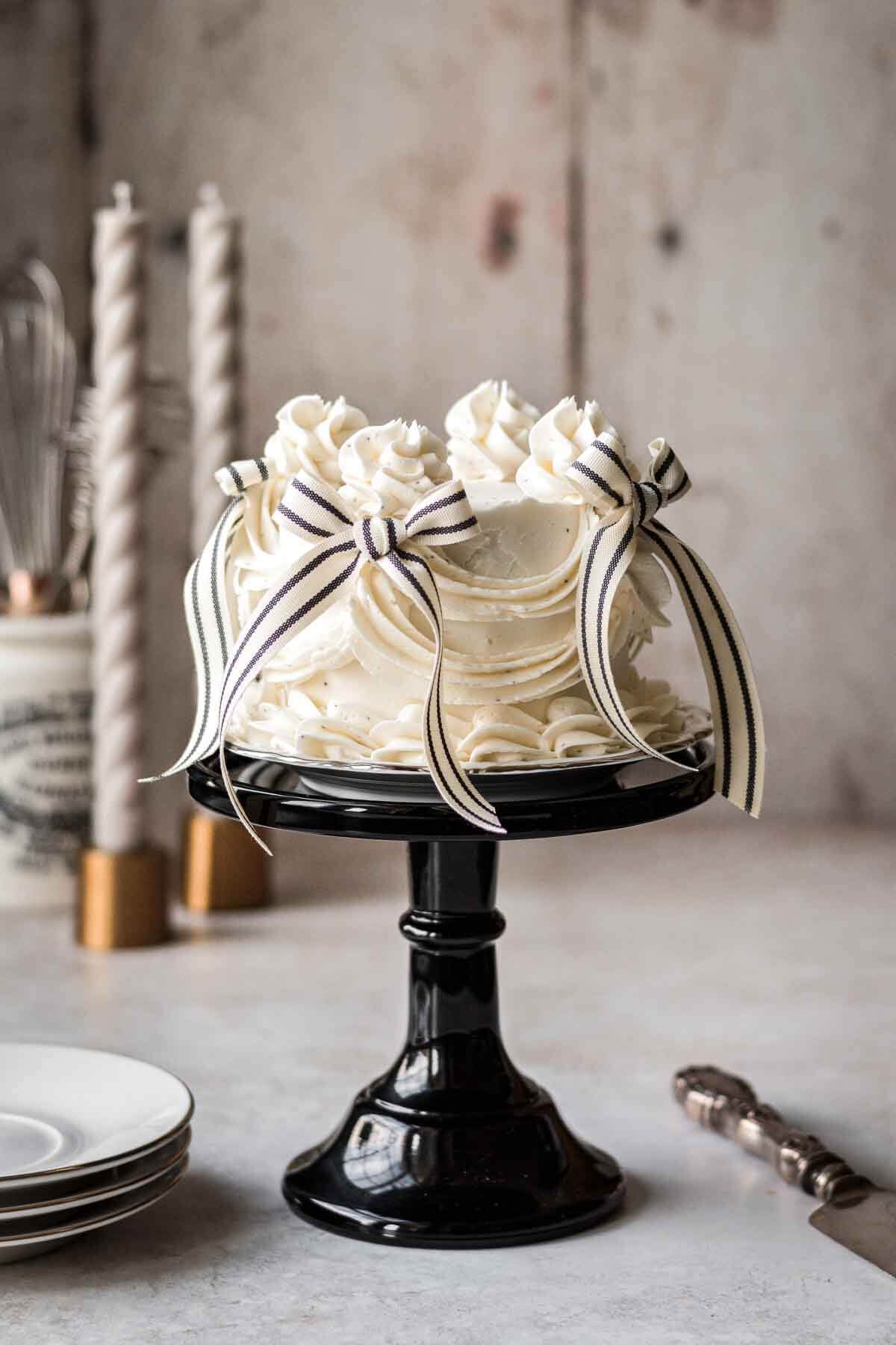 Almond poppy seed cake with vintage piping and black and white bows on a black cake stand.