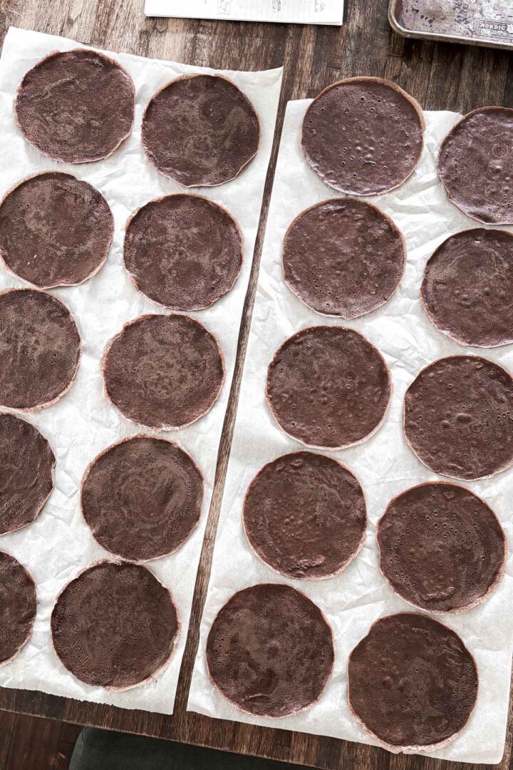 Chocolate crepes spread out on parchment paper to cool.