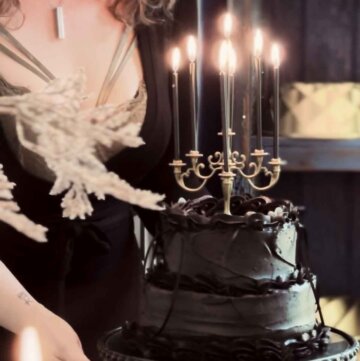 A woman standing behind a tiered black velvet cake with candles.