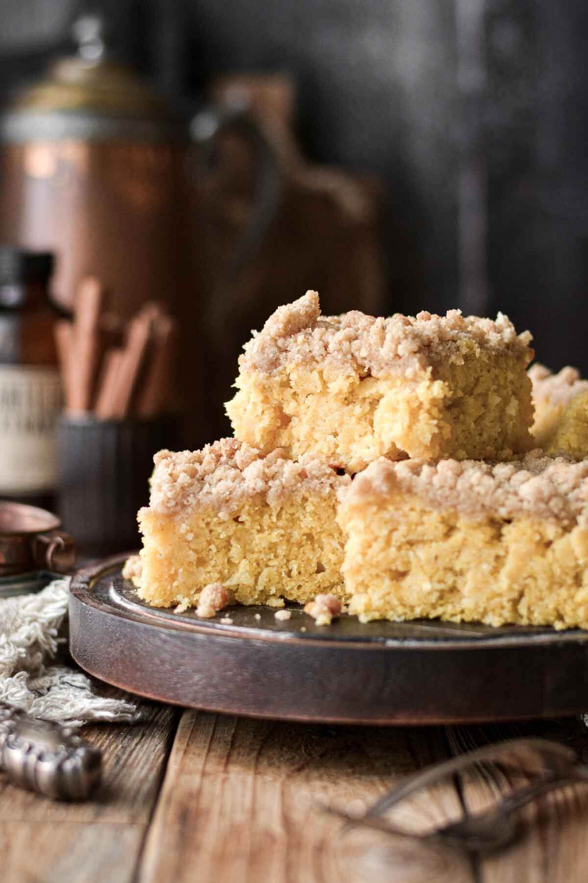 Apple cornbread cake with crumb topping stacked on a wooden plate.