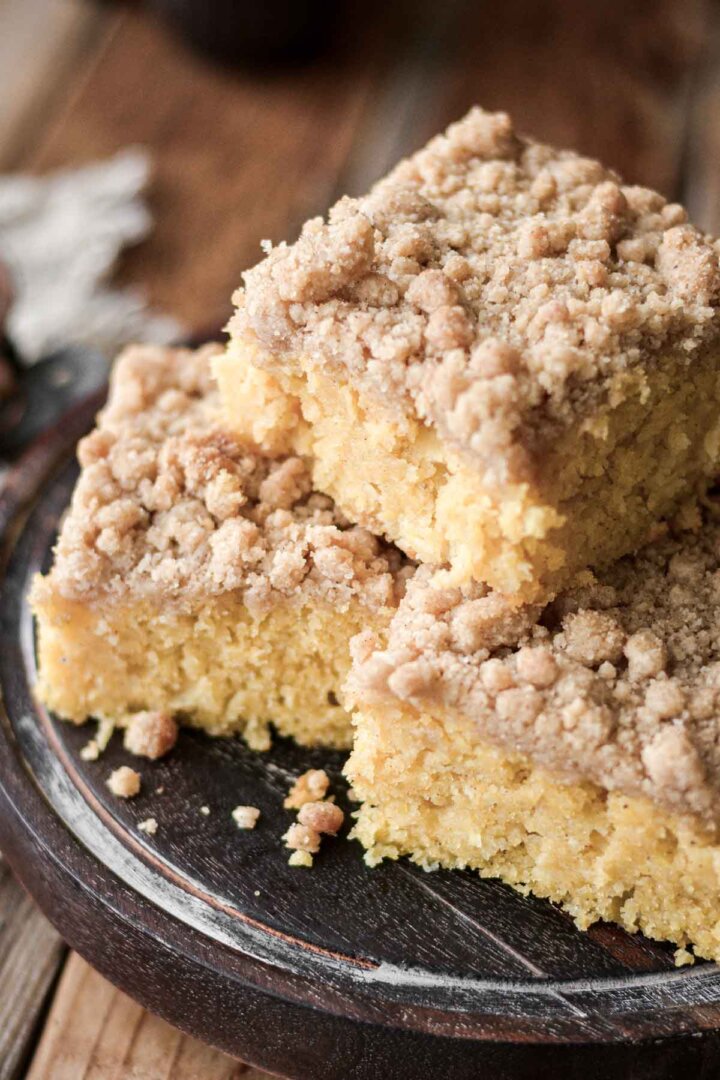 Apple cornbread cake with crumb topping stacked on a wooden plate.