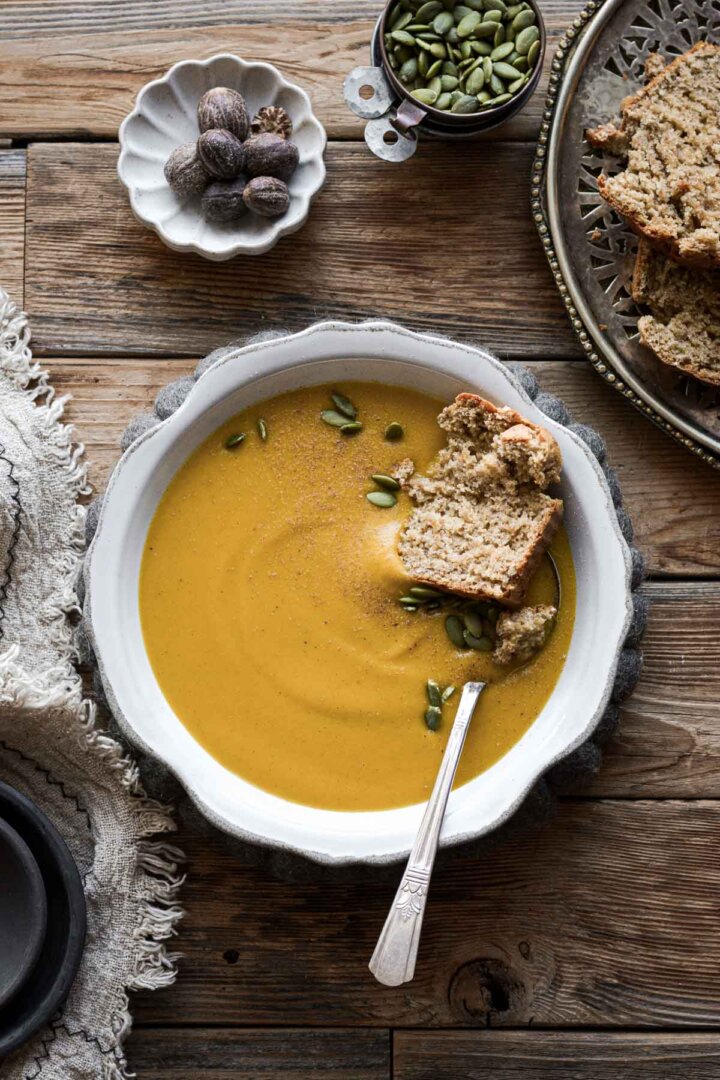 A bowl of creamy butternut squash soup with pumpkin seeds and crusty bread.