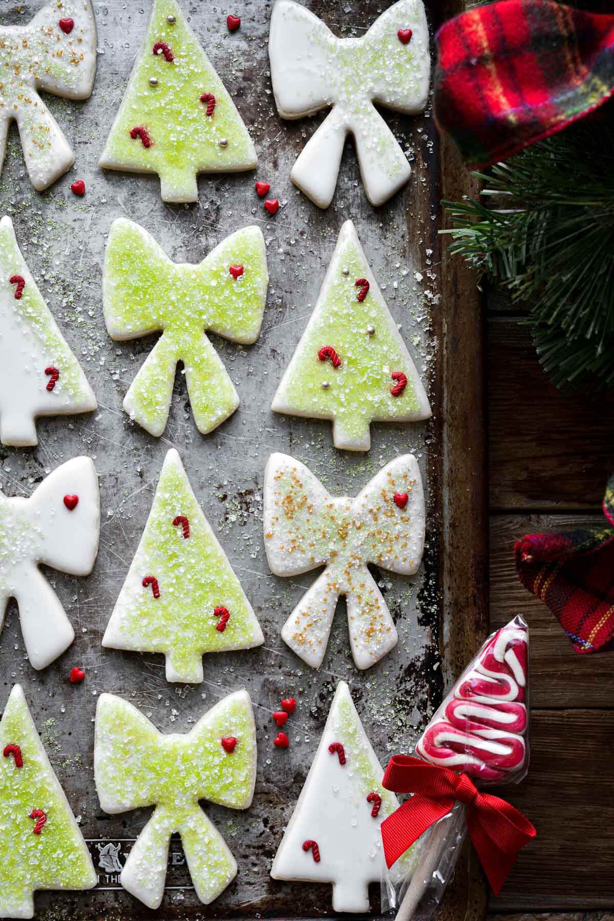 Grinch inspired cutout cookies, cut in tree and bow shapes, with white icing, green sugar, red hearts and candy cane sprinkles.