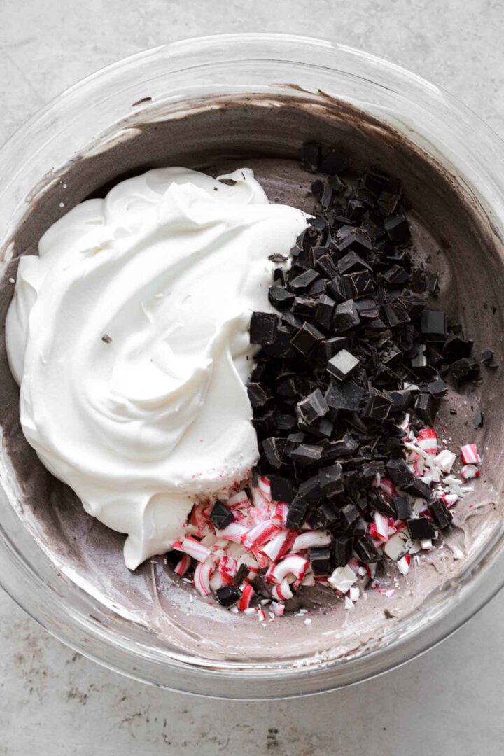Step 5 for making chocolate peppermint ice cream - adding more whipped cream, chopped chocolate and peppermints.