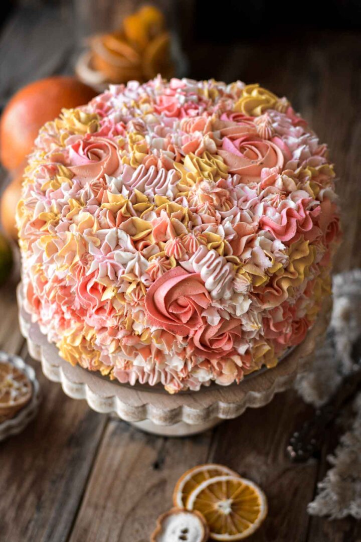 A citrus cake decorated with piped floral buttercream in shades of pink, yellow, orange and white.