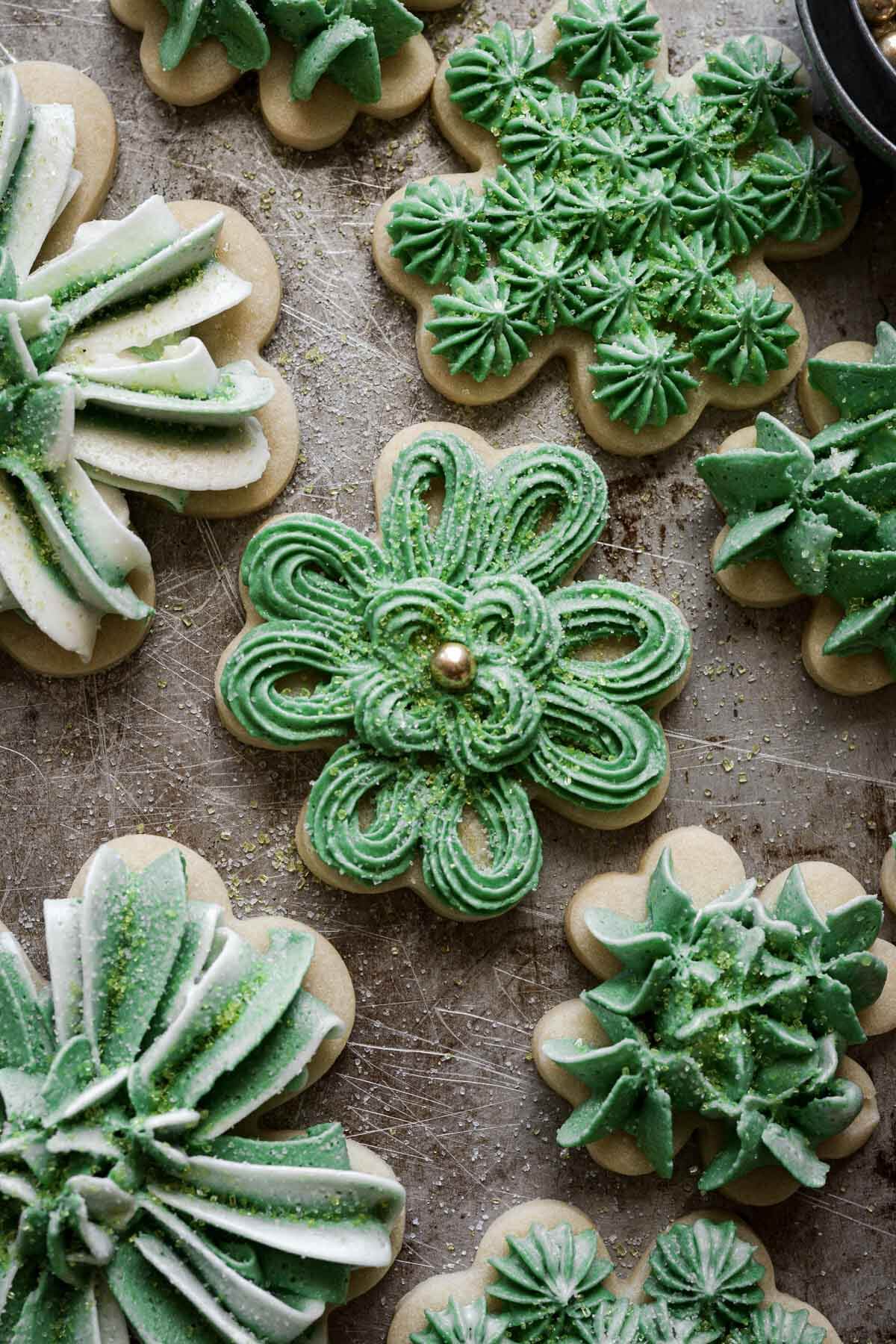Four leaf clover cutout cookies decorated with green and white buttercream and gold sprinkles for St Patrick's Day.