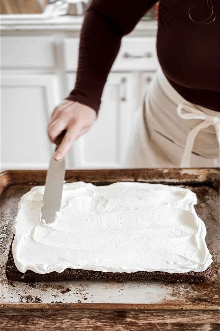 Spreading whipped vanilla buttercream onto a chocolate cake.