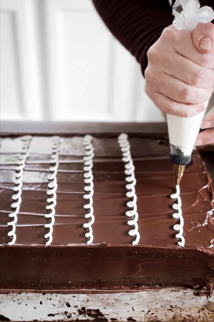 Piping vanilla icing onto a chocolate cake.