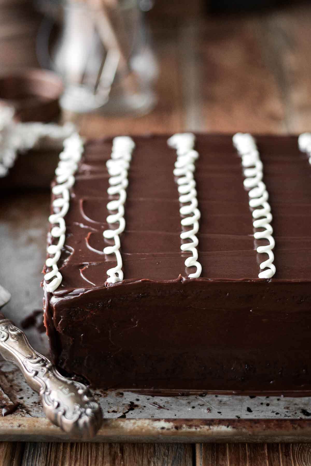 Chocolate sheet cake with ganache and curly white icing on top.