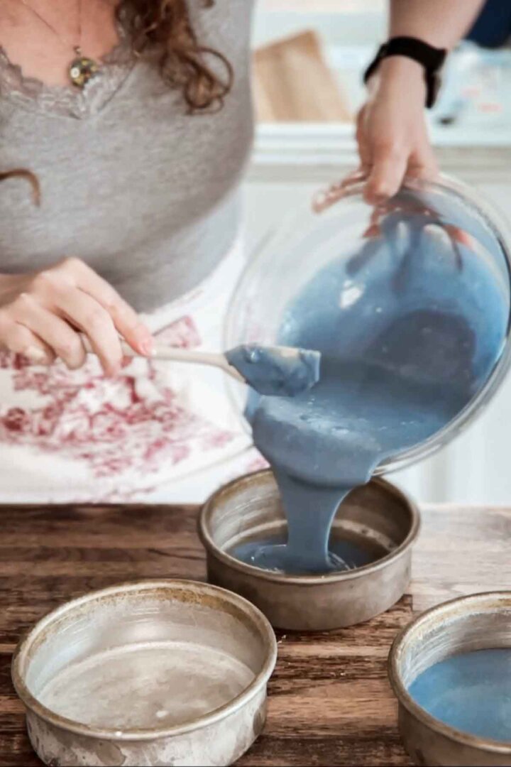 Pouring blue cake batter into cake pans.