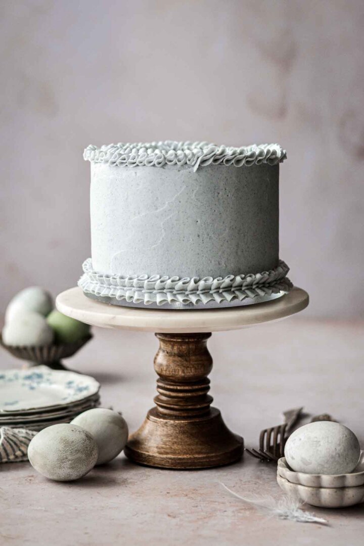 Pale blue frosted layer cake on a marble and wood cake stand.