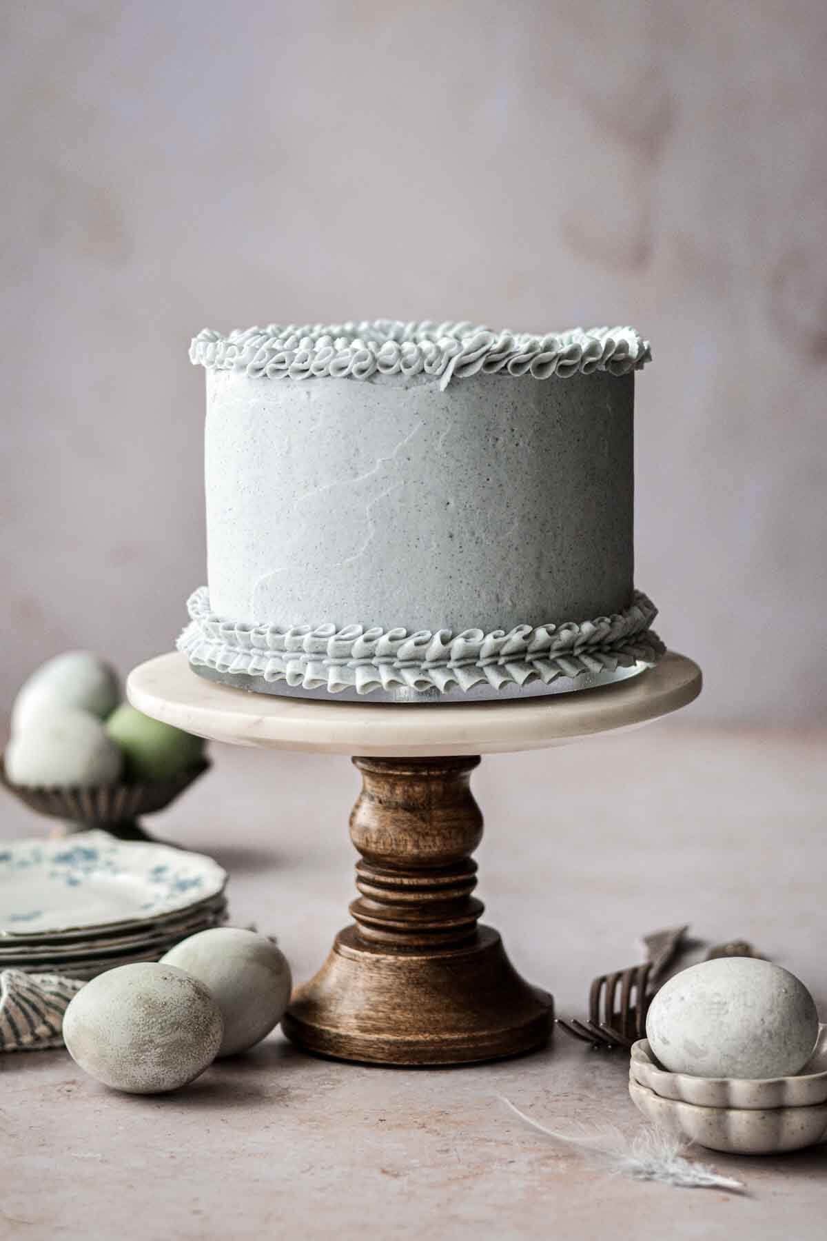 Pale blue frosted layer cake on a marble and wood cake stand.
