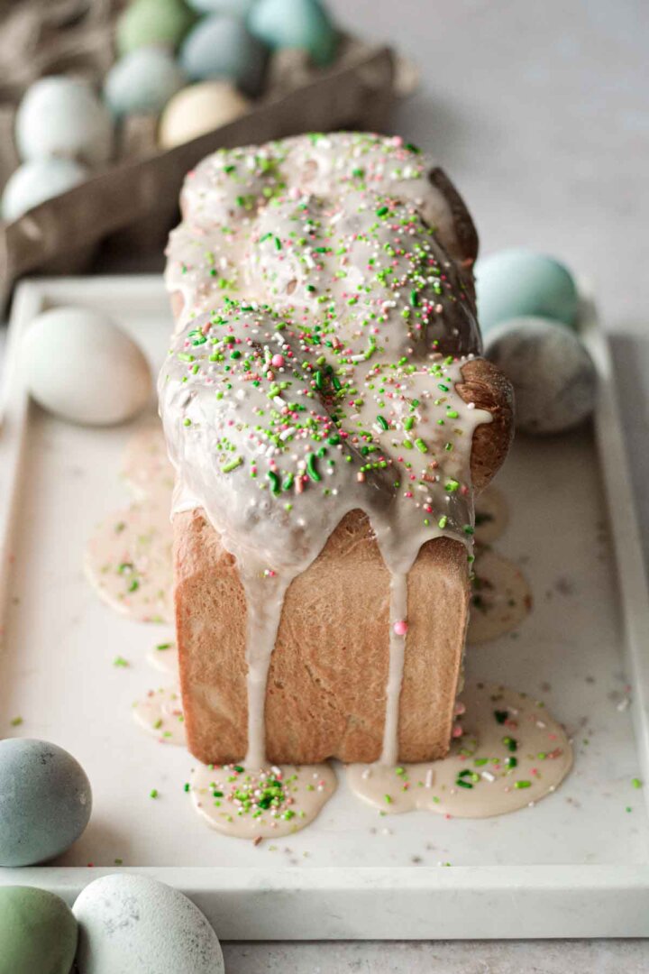 Loaf of Easter bread with icing and sprinkles, surrounded by dyed eggs.