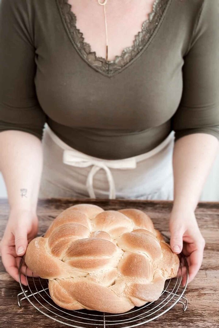Woman holding braided bread loaf on a cooling rack.
