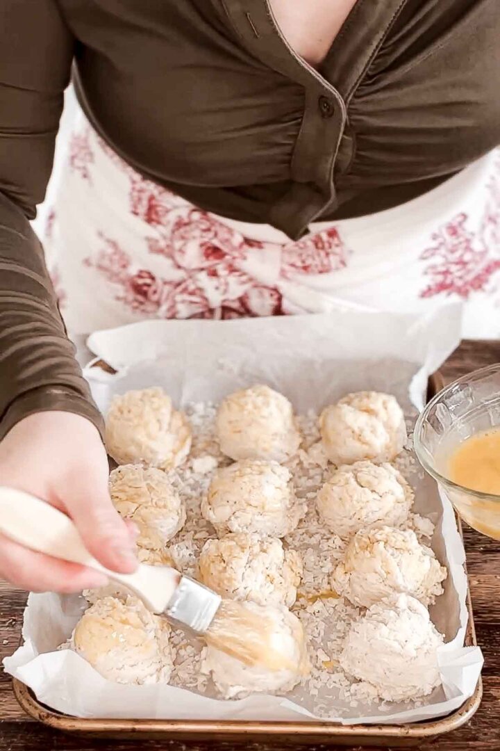 Brushing egg wash over biscuits.