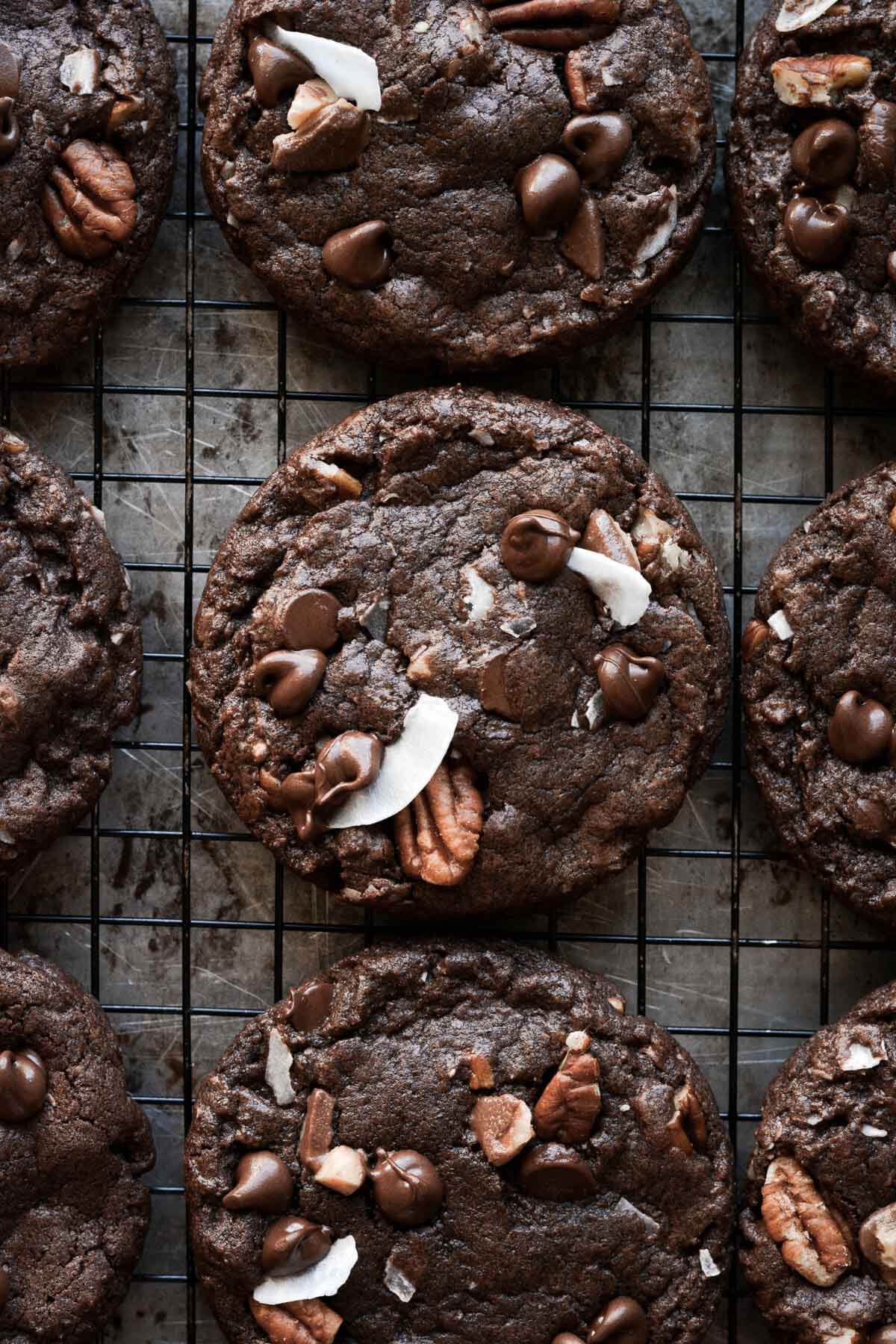 German chocolate cookies on a cooling rack, topped with pecans, coconut, chocolate chips and toffee bits.