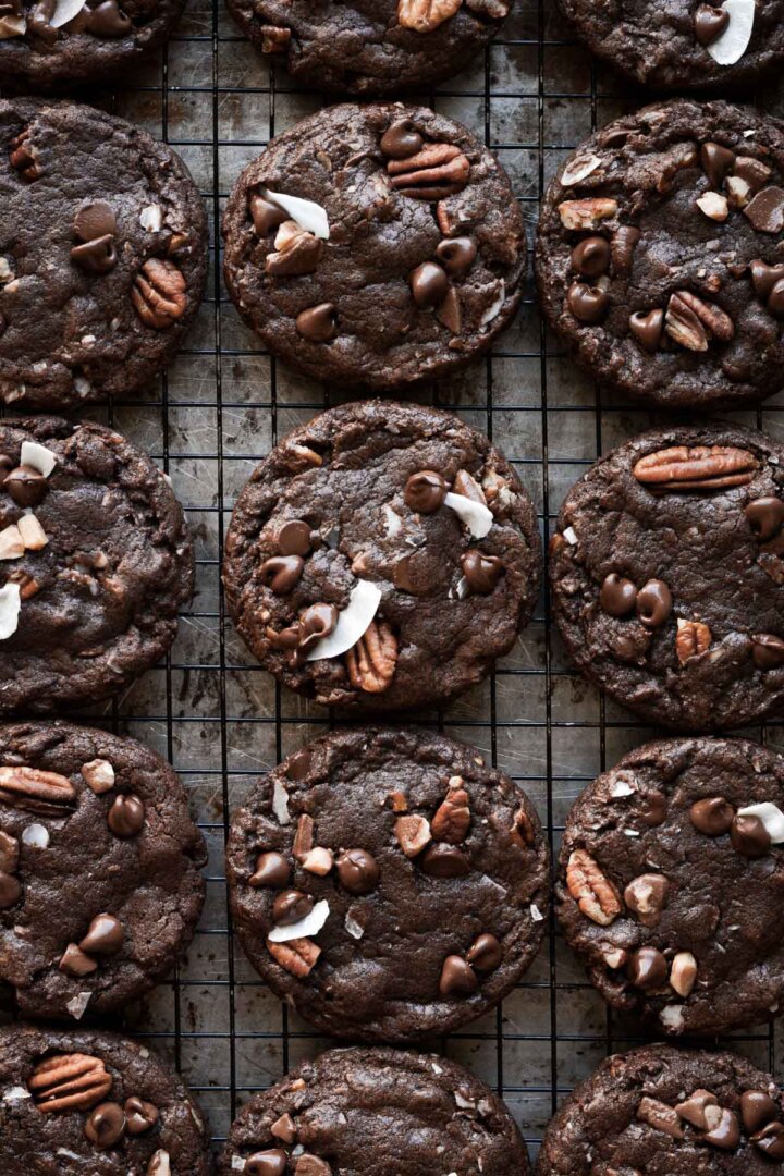 German chocolate cookies on a cooling rack, topped with pecans, coconut, chocolate chips and toffee bits.