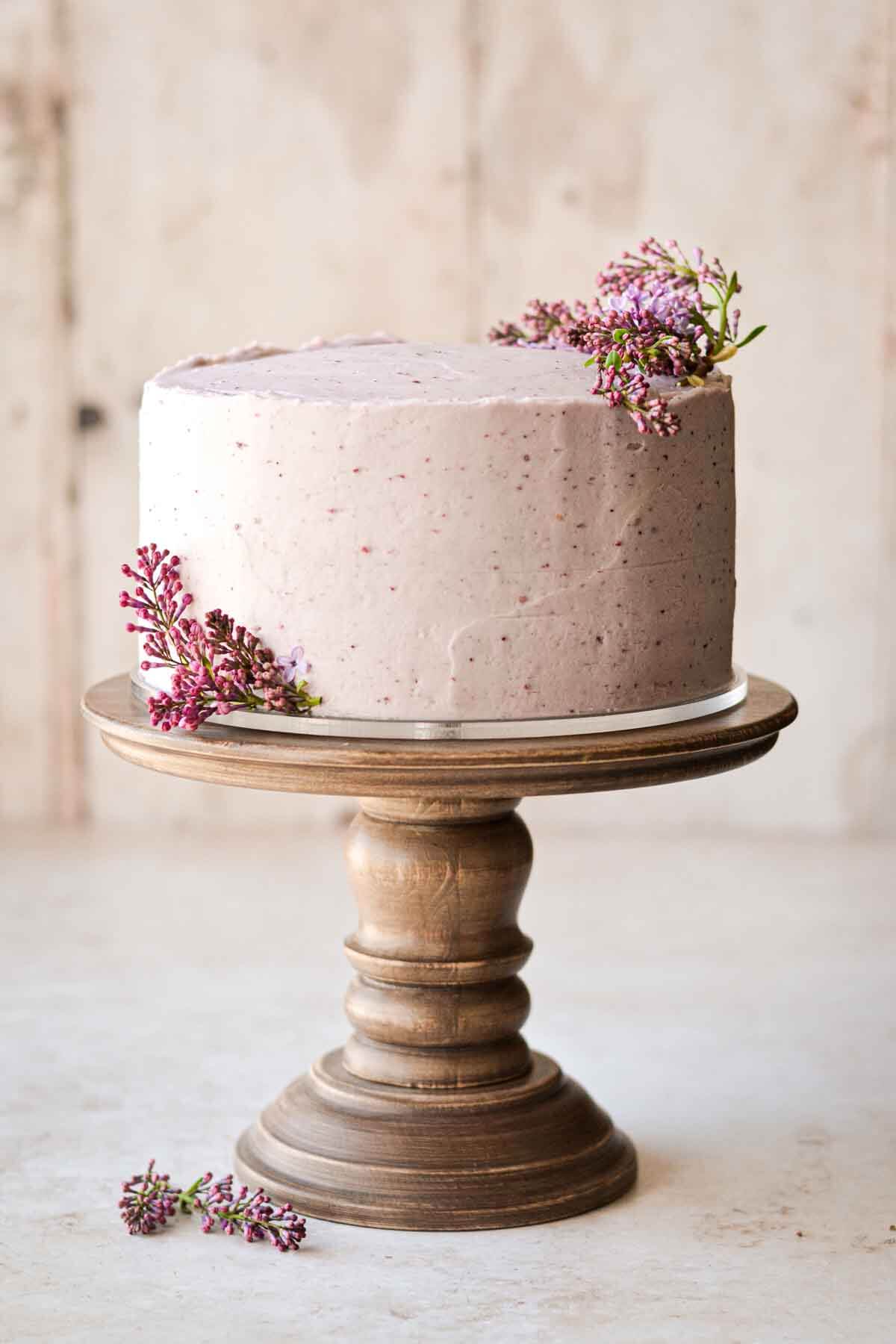 Fresh lilacs on a layer cake, sitting on a wooden cake stand.