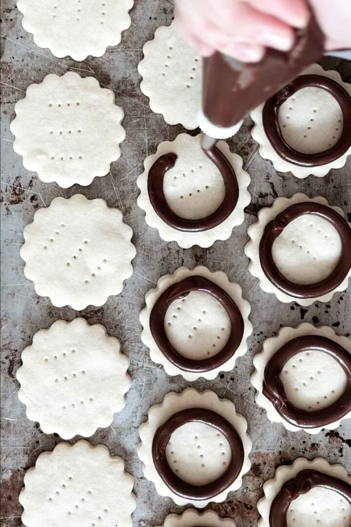 Piping a ring of chocolate ganache onto shortbread cookies.