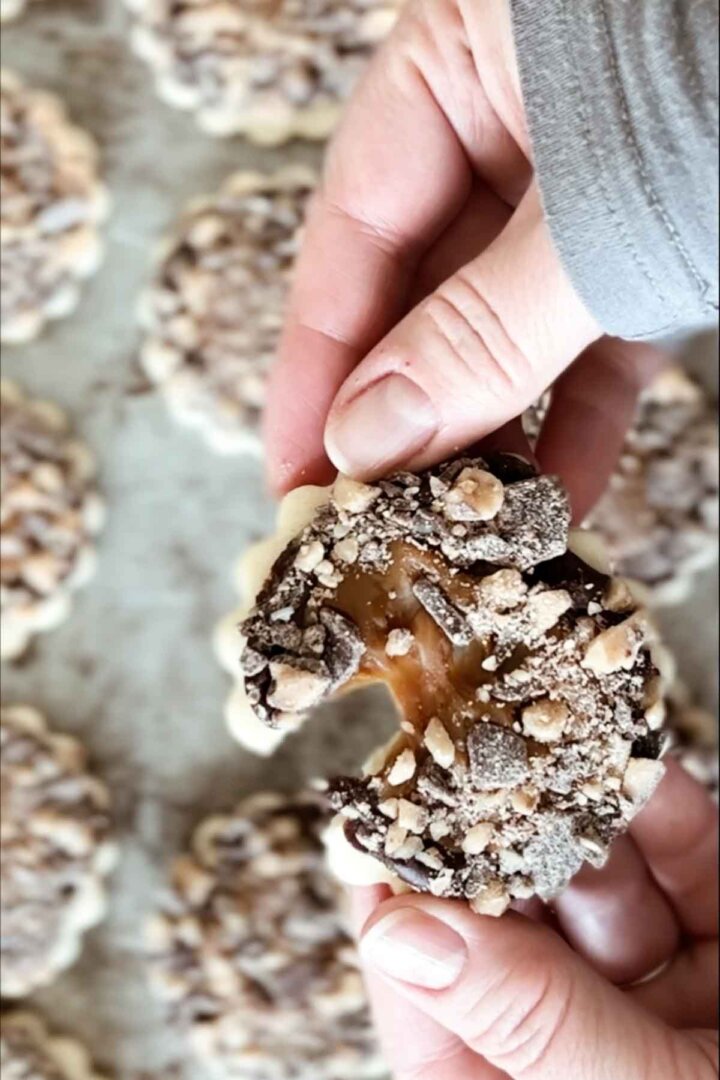 A cookie being broken in half to show the sticky caramel in the middle.