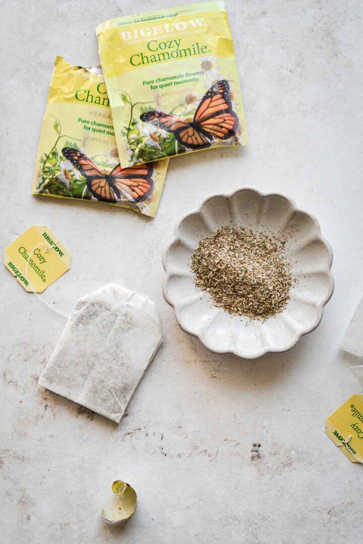 Chamomile tea bags, one opened and poured into a small dish.