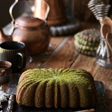 Matcha loaf cake, sprinkled with green sugar, on a black cutting board.