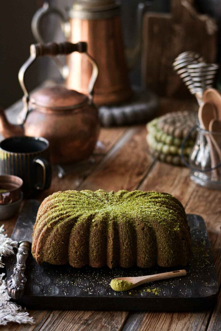 Matcha loaf cake, sprinkled with green sugar, on a black cutting board.