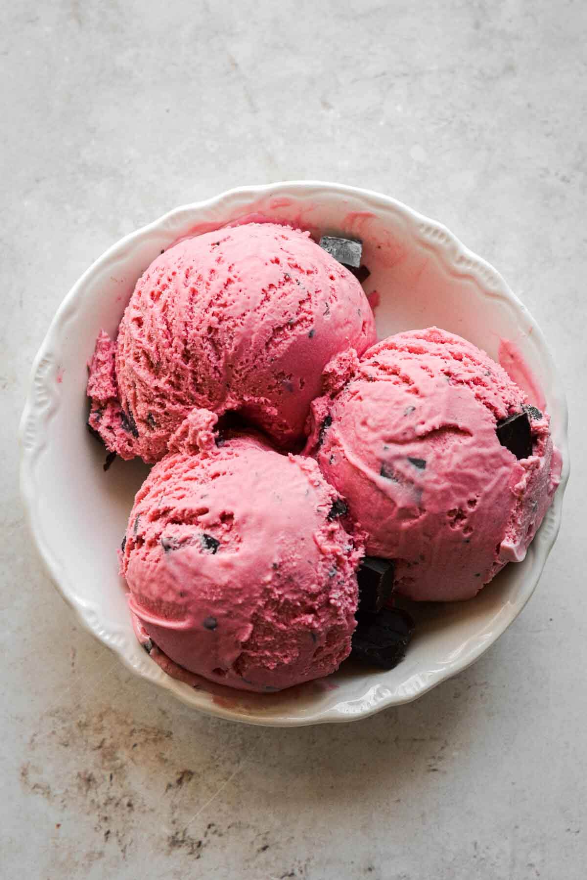 Scoops of homemade raspberry chocolate chunk ice cream in a bowl.
