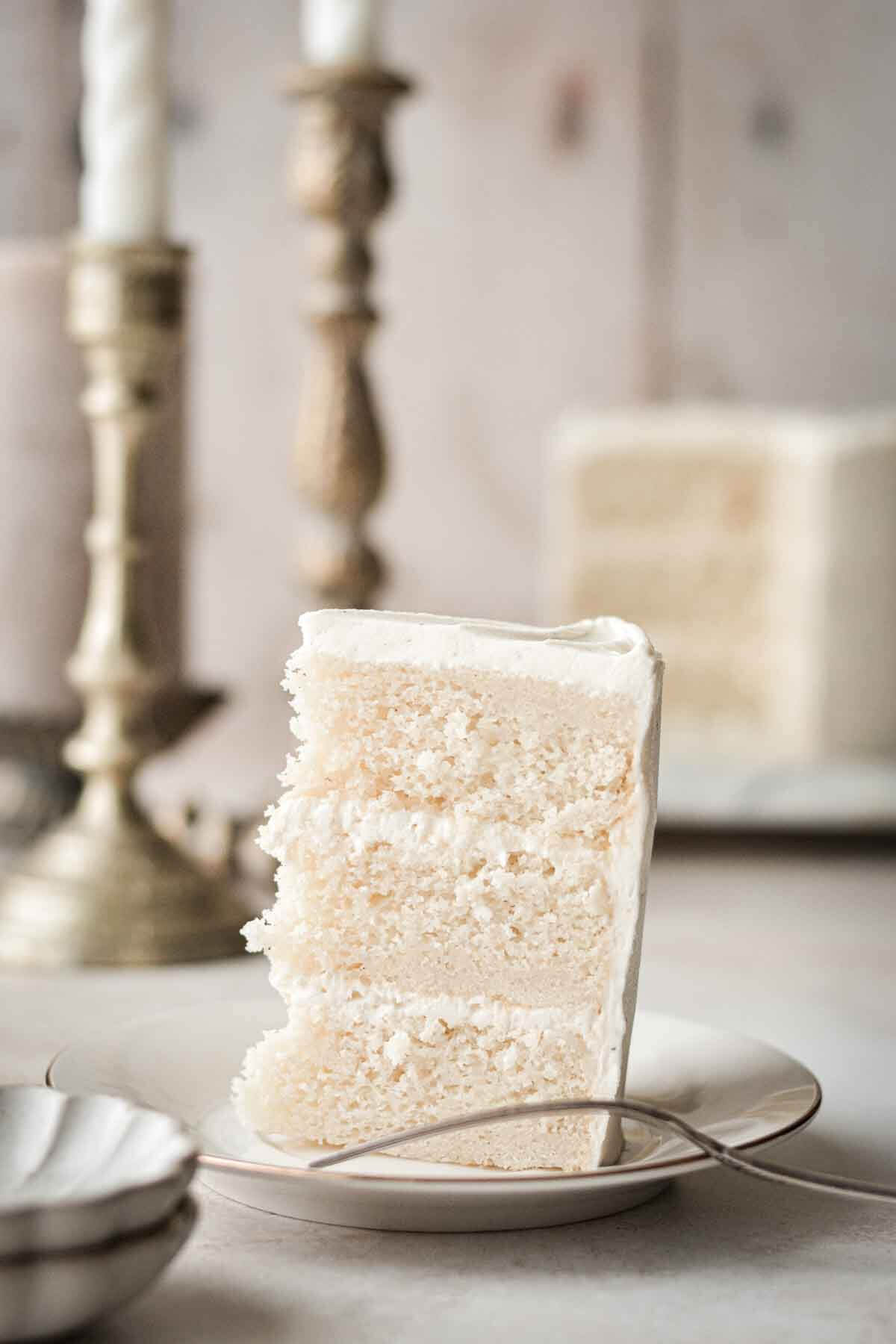 Slice of white velvet cake with gold candlesticks in the background.