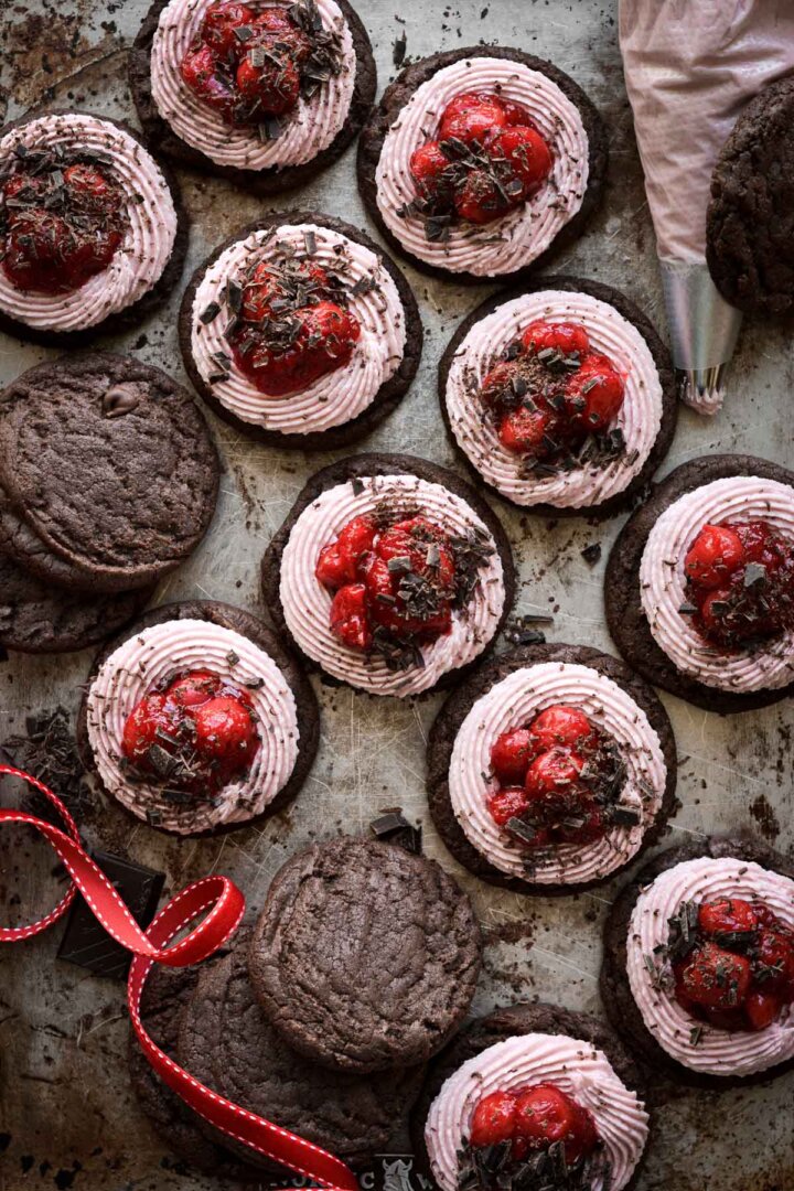 Chocolate brownie cookies with pink buttercream, cherry pie filling and chopped chocolate.
