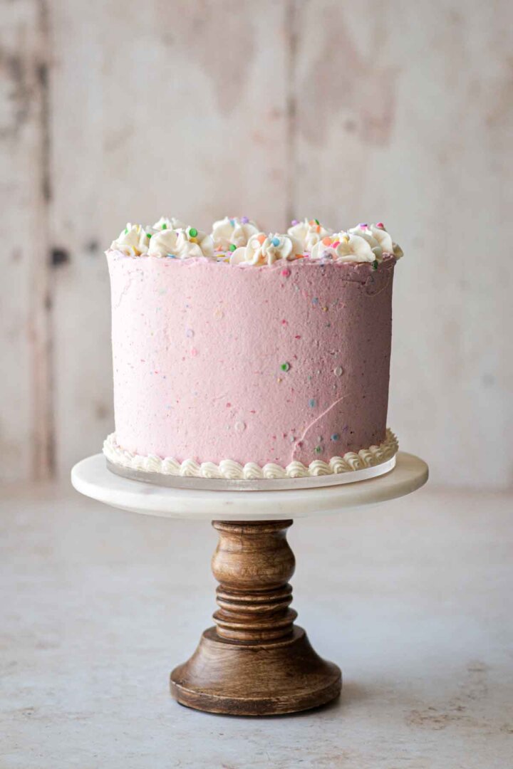 Birthday cake with pink and white buttercream on a cake stand.