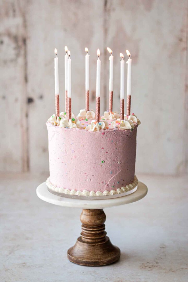 Pink and white birthday cake topped with candles.