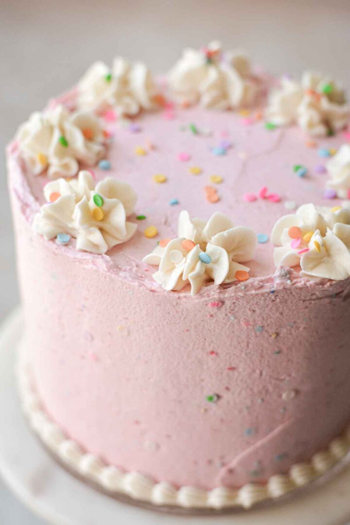 Gluten free vanilla birthday cake with pink buttercream, white piping, and sprinkles.