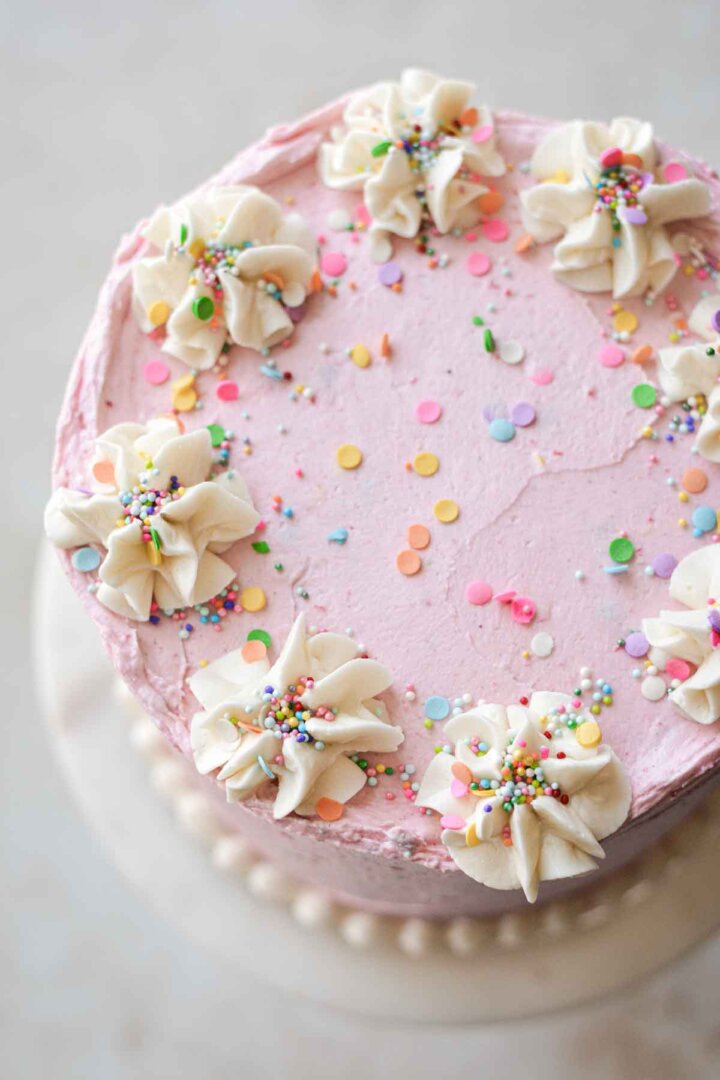 Gluten free vanilla birthday cake with pink buttercream, white piping, and sprinkles.