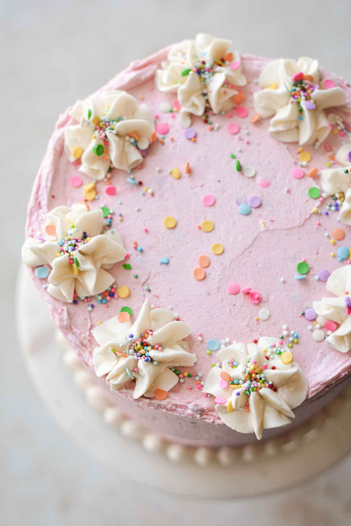Gluten free vanilla birthday cake with pink buttercream, white piping, and sprinkles.