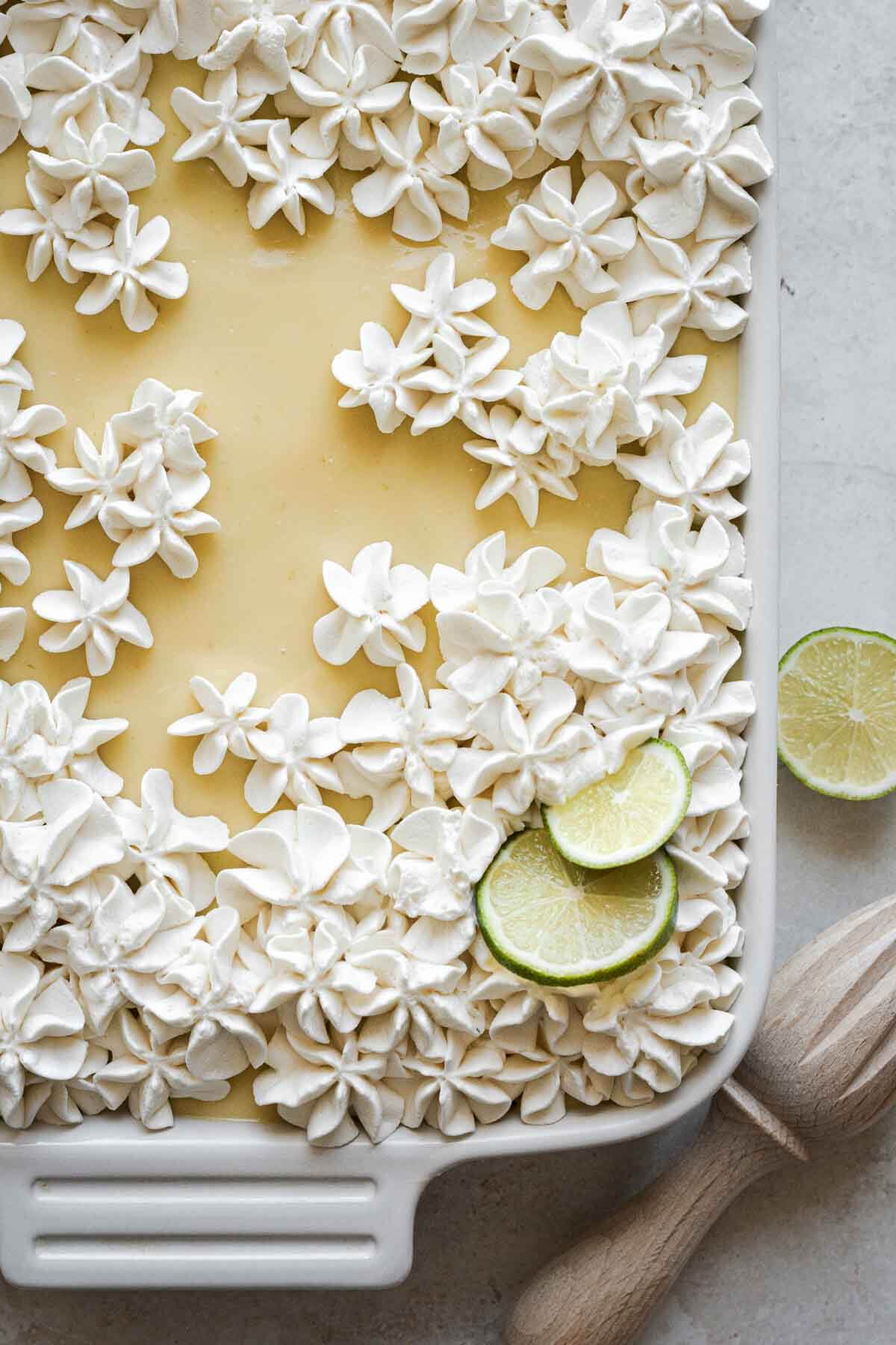 Key lime pie sheet cake with whipped cream flowers and lime slices on top.