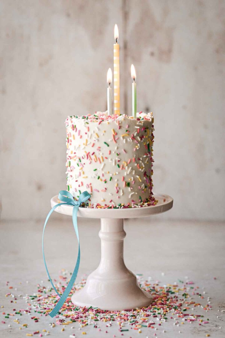 Mini confetti cake with sprinkles scattered around, decorated with a blue ribbon and birthday candles.