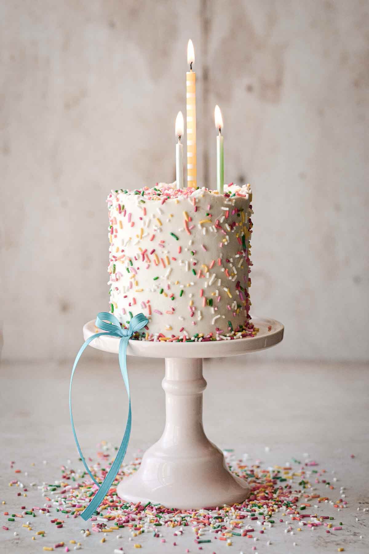 Mini confetti cake with sprinkles scattered around, decorated with a blue ribbon and birthday candles.