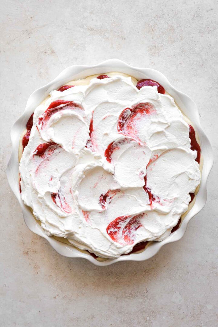 Layered strawberry pudding in a white pie pan, topped with swirls of strawberry whipped cream.