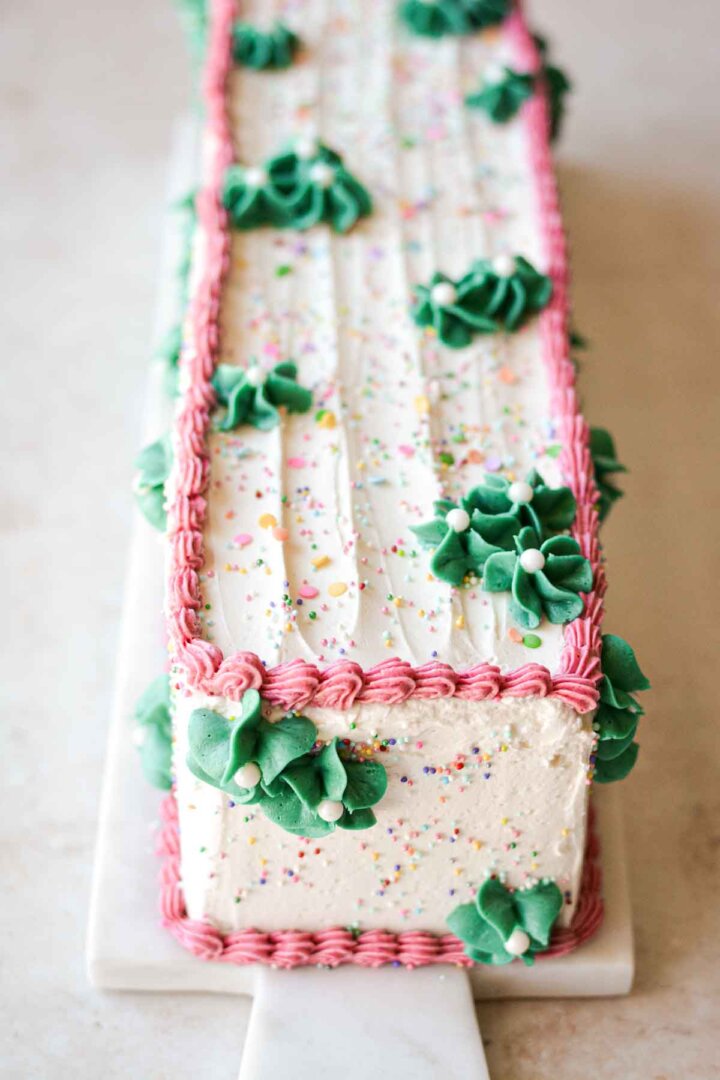 Table runner birthday cake, with sprinkles, pink buttercream piping, and green buttercream flowers.