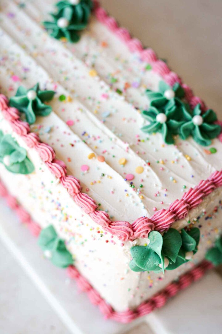 Table runner birthday cake, with sprinkles, pink buttercream piping, and green buttercream flowers.