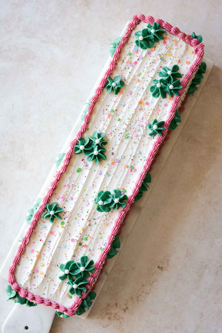 Table runner birthday cake, with sprinkles, pink buttercream piping, and green buttercream flowers.