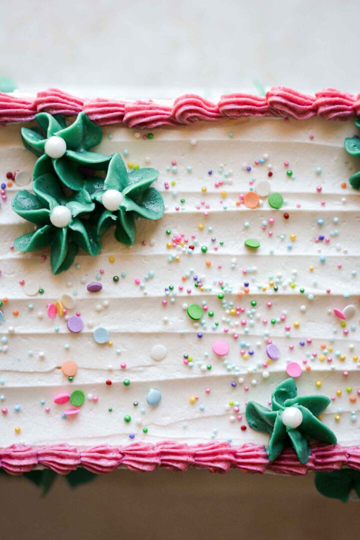 Table runner birthday cake, with sprinkles, pink buttercream piping, and green buttercream flowers.