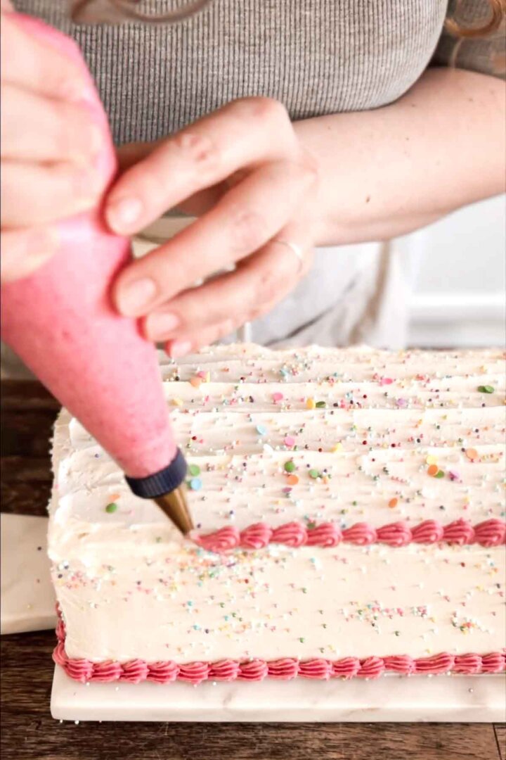 Step 7 for assembling a table runner cake - adding piped pink buttercream around edges.