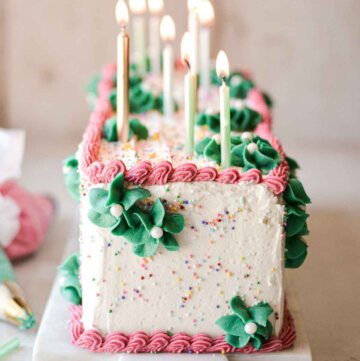 Table runner birthday cake with sprinkles, pink and green buttercream, and birthday candles.